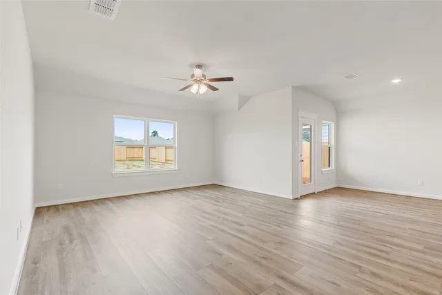 an empty room with wooden floor chandelier fan and windows