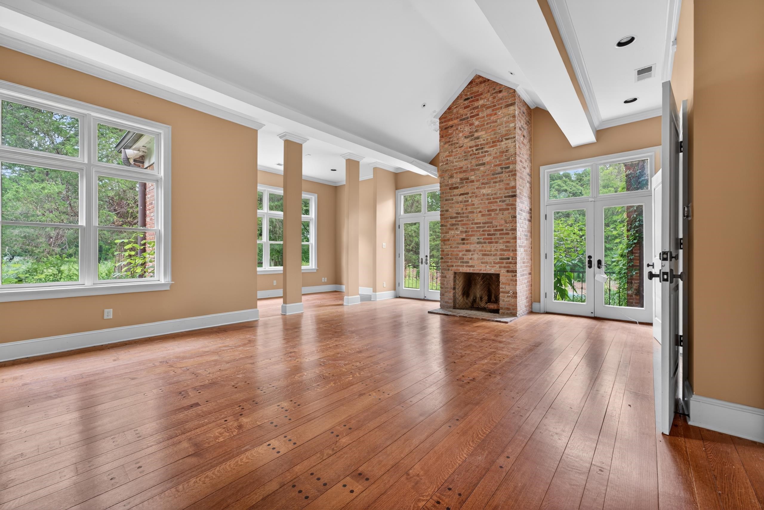 530 West Raines Road Memphis, TN 38109 - Photo 33 of 38 Spacious living area featuring a vaulted ceiling, prominent brick fireplace, wood-finish flooring, multiple large windows, and double French doors to the exterior