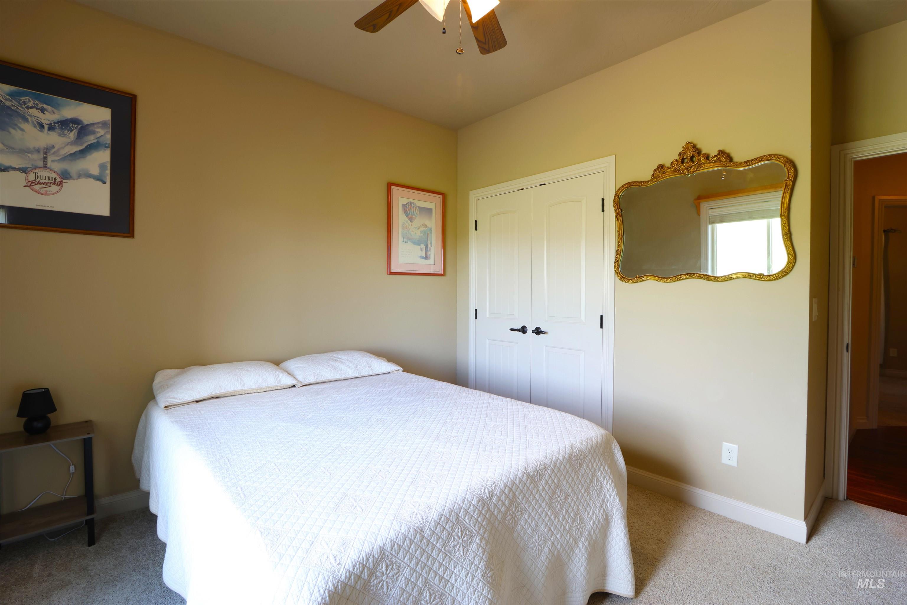 2278 Golf Lane Council, ID 83612 - Photo 19 of 31 Neutral wall color, light-colored carpet flooring, white bi-fold closet doors with black hardware, ornate gold-framed wall mirror, and a ceiling fan with wood-finish blades