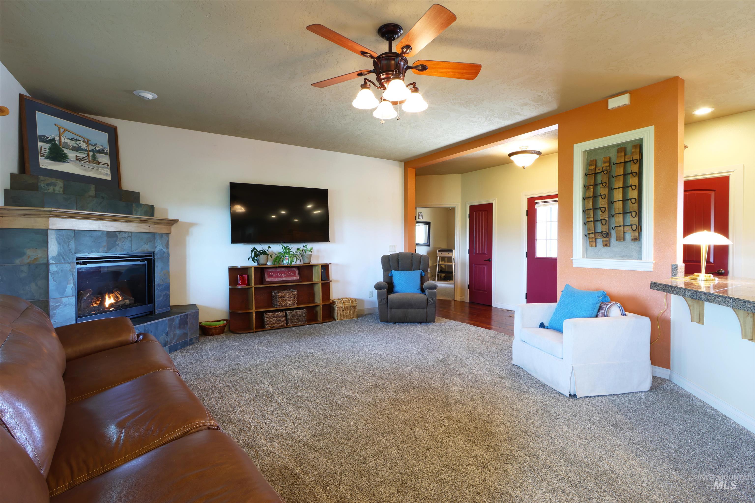 2278 Golf Lane Council, ID 83612 - Photo 5 of 31 Spacious living area featuring a stone-clad fireplace with mantel, ceiling fan with light fixture, carpeted flooring, and a partial wall separating spaces