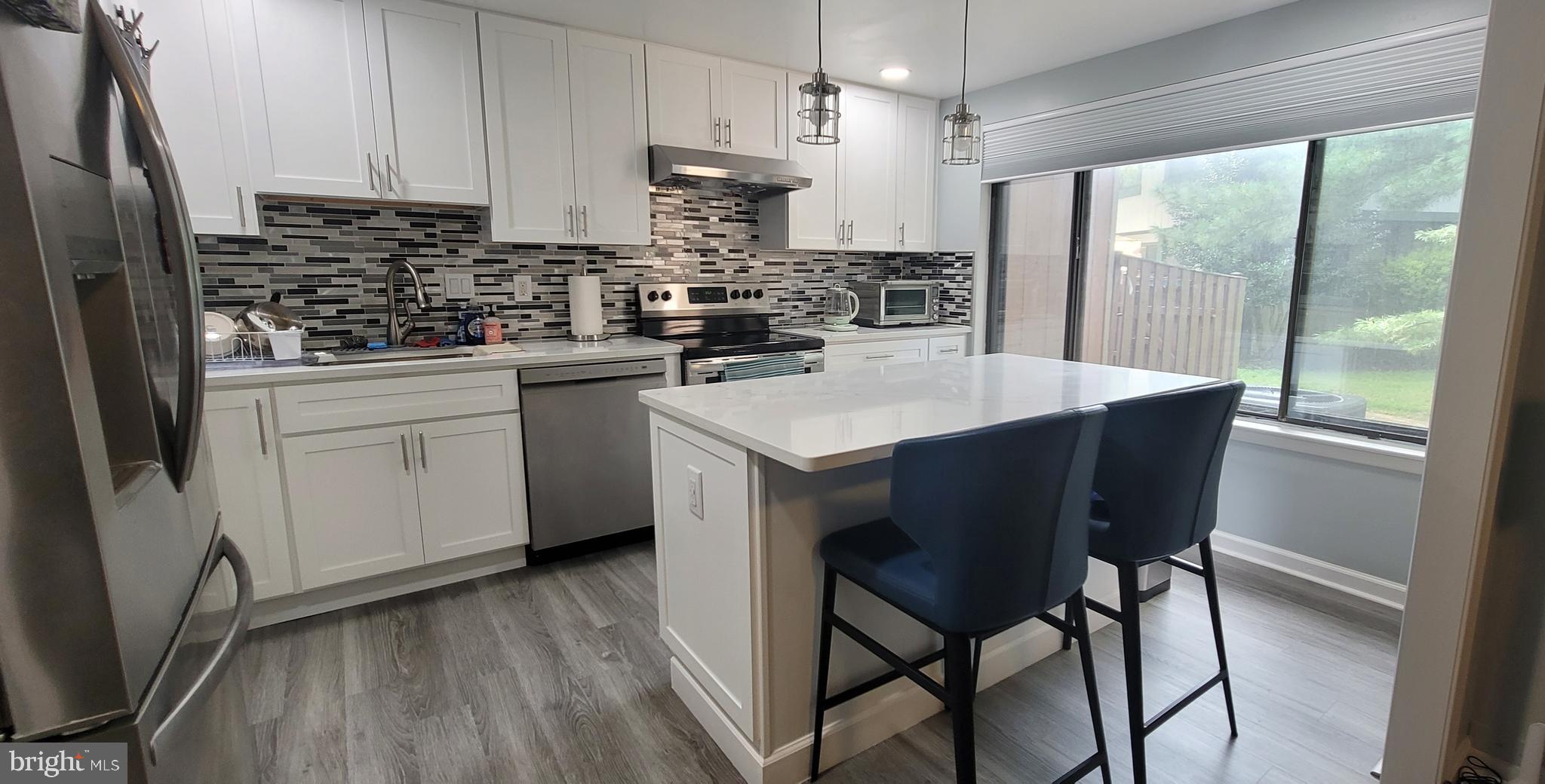 a kitchen with stainless steel appliances granite countertop a table chairs refrigerator a sink and white cabinets