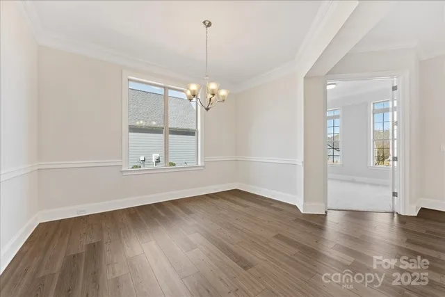 an empty room with wooden floor chandelier and windows