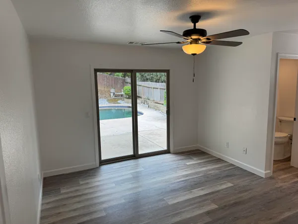 an empty room with wooden floor fan and windows