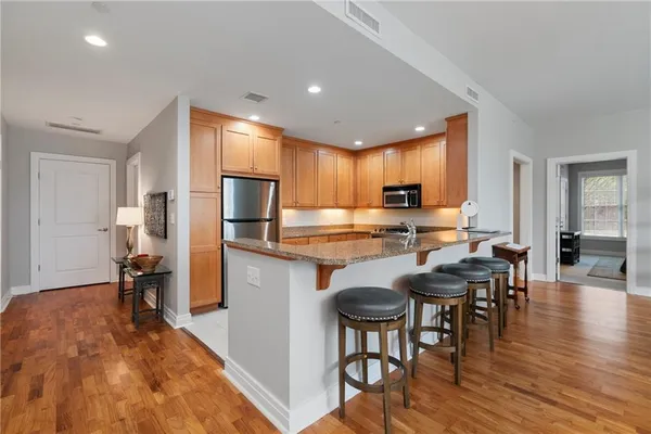 a kitchen with stainless steel appliances granite countertop a refrigerator a stove a sink a dining table and chairs with wooden floor