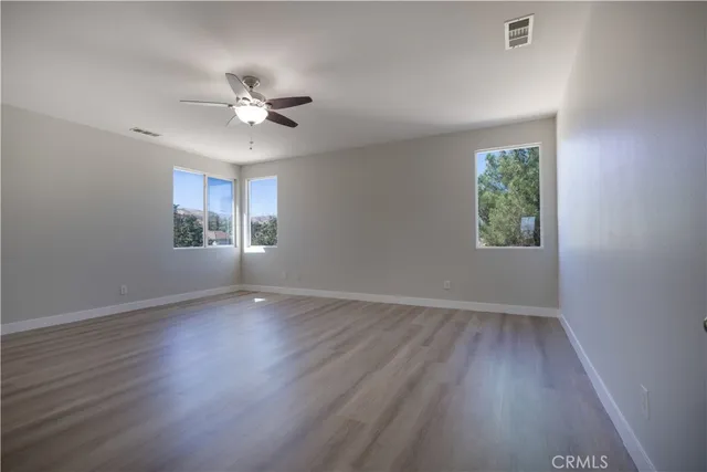 an empty room with wooden floor chandelier fan and windows