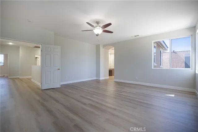 a view of an empty room with wooden floor and a ceiling fan
