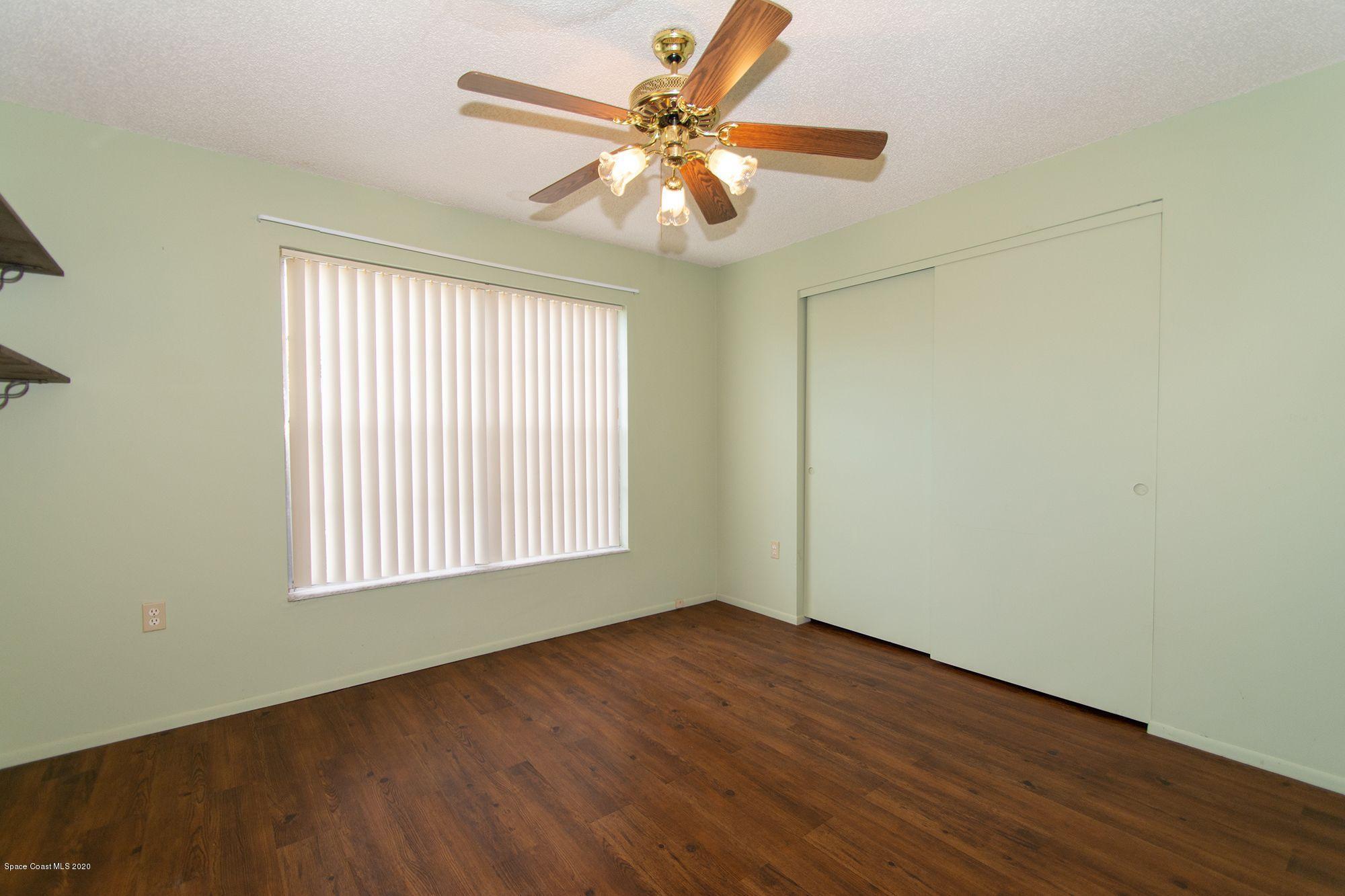 2872 Pembroke Road Melbourne, FL 32935 - Photo 32 of 32 an empty room with wooden floor chandelier fan and windows