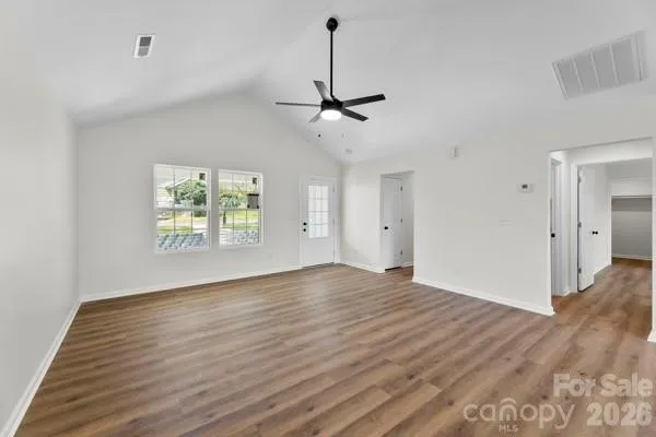 an empty room with wooden floor ceiling fan and windows