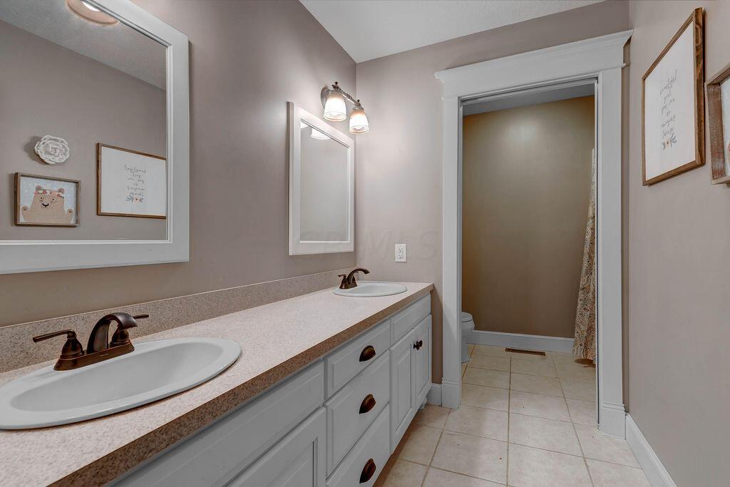 4045 Russell Road Mount Gilead, OH 43338 - Photo 34 of 74 • Neutral tile flooring • Tan painted walls • Double sink with mirrors • Two lights over mirrors • New faucets • White cabinets • Shower/toilet room