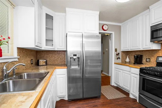 a kitchen with stainless steel appliances granite countertop a refrigerator a sink and white cabinets