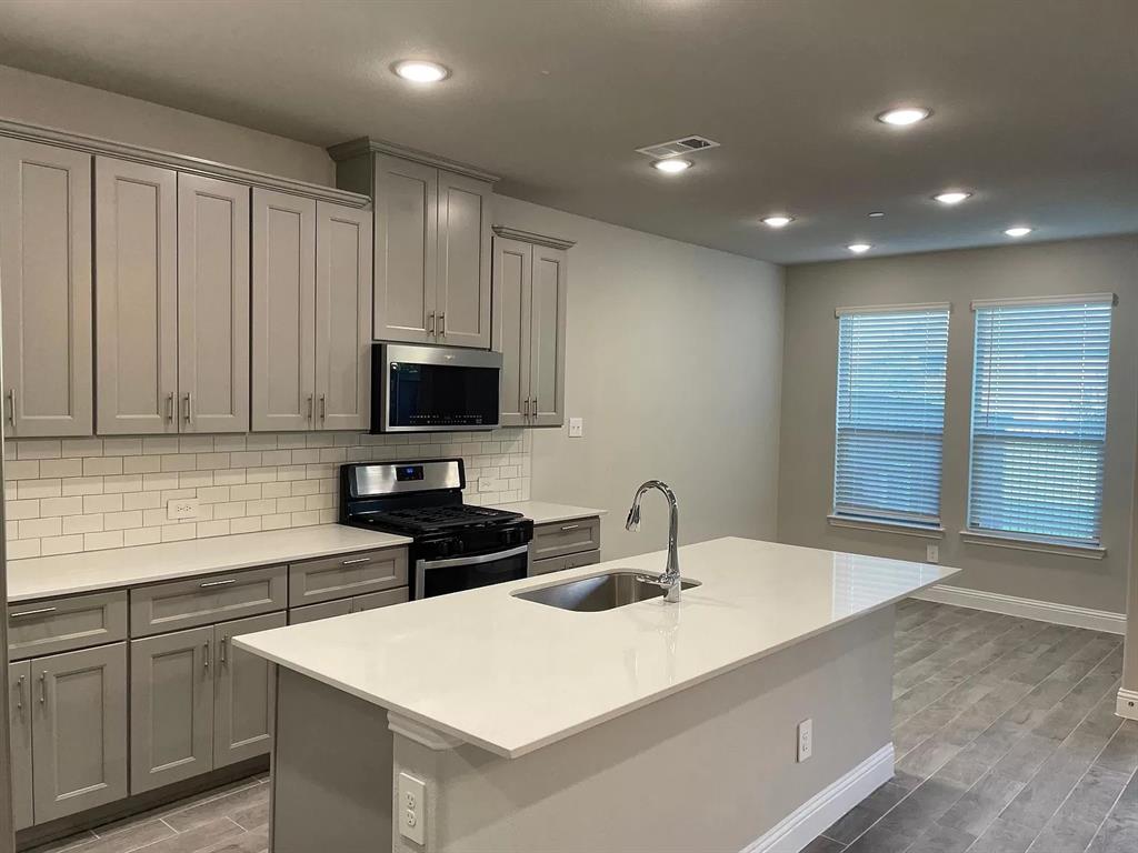 1752 Redding Street Allen, TX 75002 - Photo 7 of 24 Kitchen with tasteful backsplash, stainless steel appliances, sink, an island with sink, and wood-type flooring