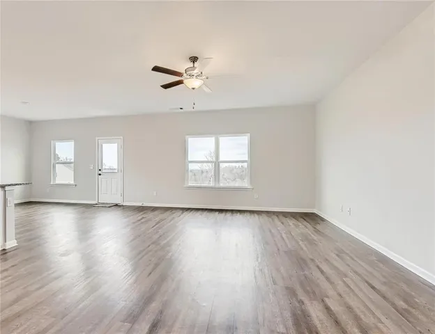 an empty room with wooden floor fan and windows