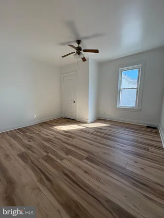 an empty room with wooden floor ceiling fan and windows
