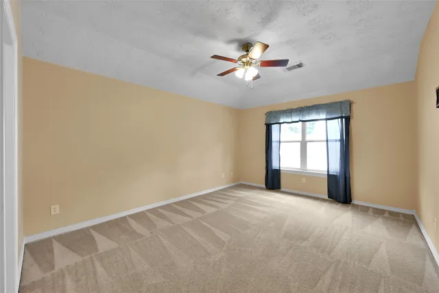 a view of an empty room with chandelier fan and a window