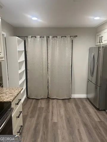 an empty room with wooden floor kitchen view and a window