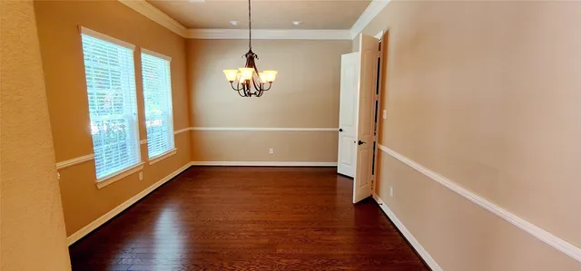 an empty room with wooden floor chandelier and windows