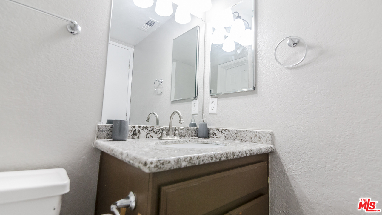 2985 North Chestnut Street Rialto, CA 92376 - Photo 15 of 30 a bathroom with a granite countertop sink a toilet and a mirror