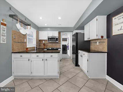 a kitchen with kitchen island granite countertop a refrigerator oven a sink and white cabinets