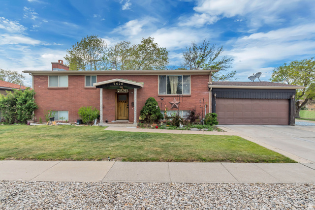 7470 Ramanee Drive Midvale, UT 84047 - Photo 2 of 29 Raised ranch featuring brick siding, a garage, driveway, a front lawn, and a chimney