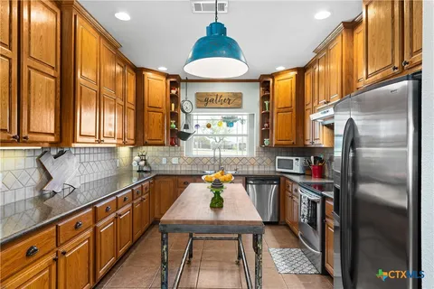 a kitchen with stainless steel appliances granite countertop a refrigerator a sink dishwasher a stove and a dining table with wooden floor