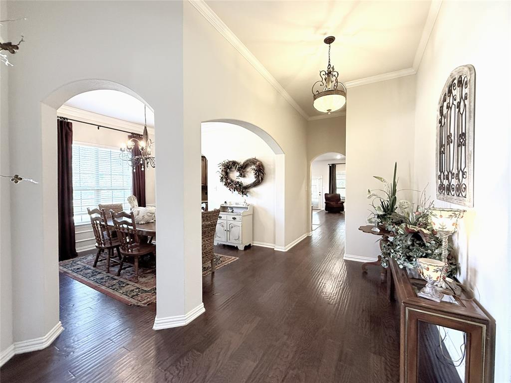 1301 Meadow Ranch Road McKinney, TX 75071 - Photo 12 of 40 Corridor with arched walkways, ornamental molding, dark wood-style flooring, healthy amount of natural light, and a chandelier