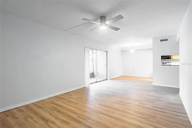 a view of an empty room with wooden floor and a ceiling fan
