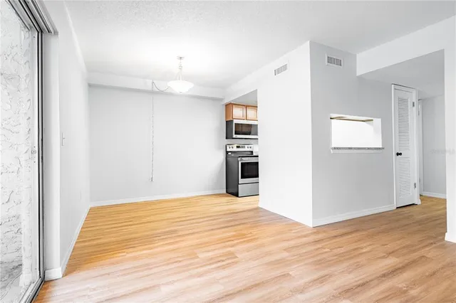 a view of empty room with wooden floor and kitchen