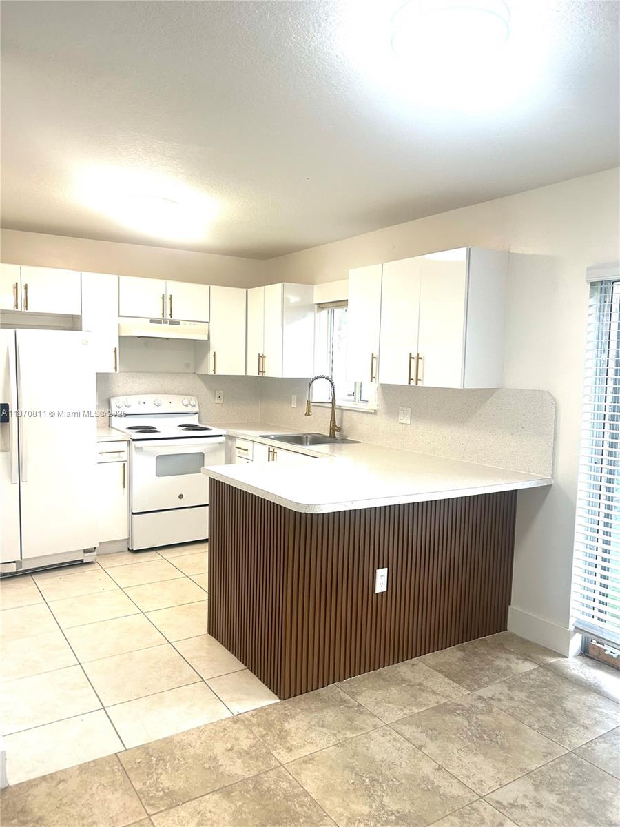 1240 Southeast 28th Court, Unit 101 Homestead, FL 33035 - Photo 6 of 20 a kitchen with a cabinets a sink a stove a refrigerator and white cabinets