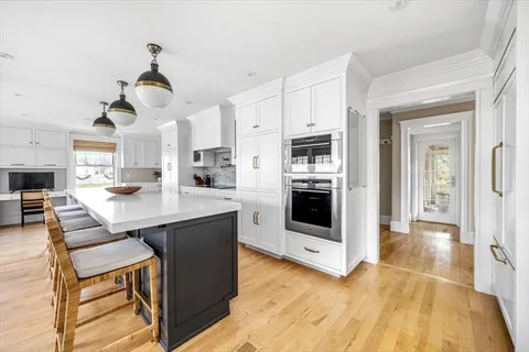 a kitchen with stainless steel appliances kitchen island granite countertop a refrigerator a stove a sink dishwasher and white cabinets with wooden floor