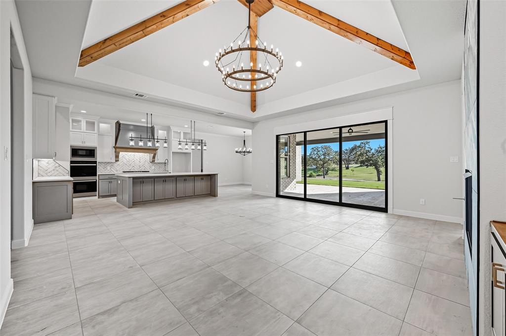 112 La Paloma Way Decatur, TX 76234 - Photo 7 of 37 Unfurnished living room with a chandelier, a raised ceiling, beamed ceiling, recessed lighting, and light tile patterned flooring
