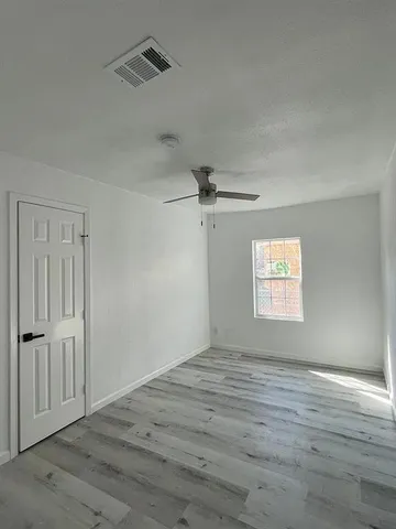 an empty room with wooden floor ceiling fan and windows