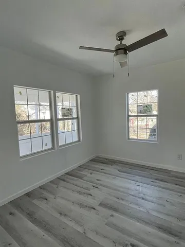 an empty room with wooden floor fan and windows