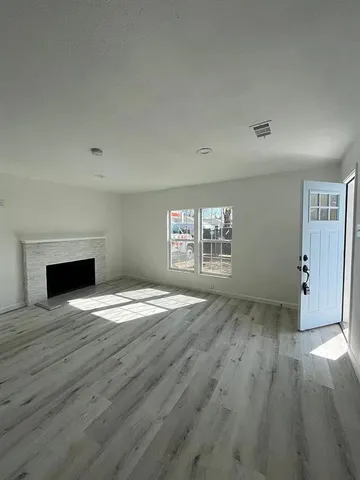 an empty room with wooden floor fireplace and windows