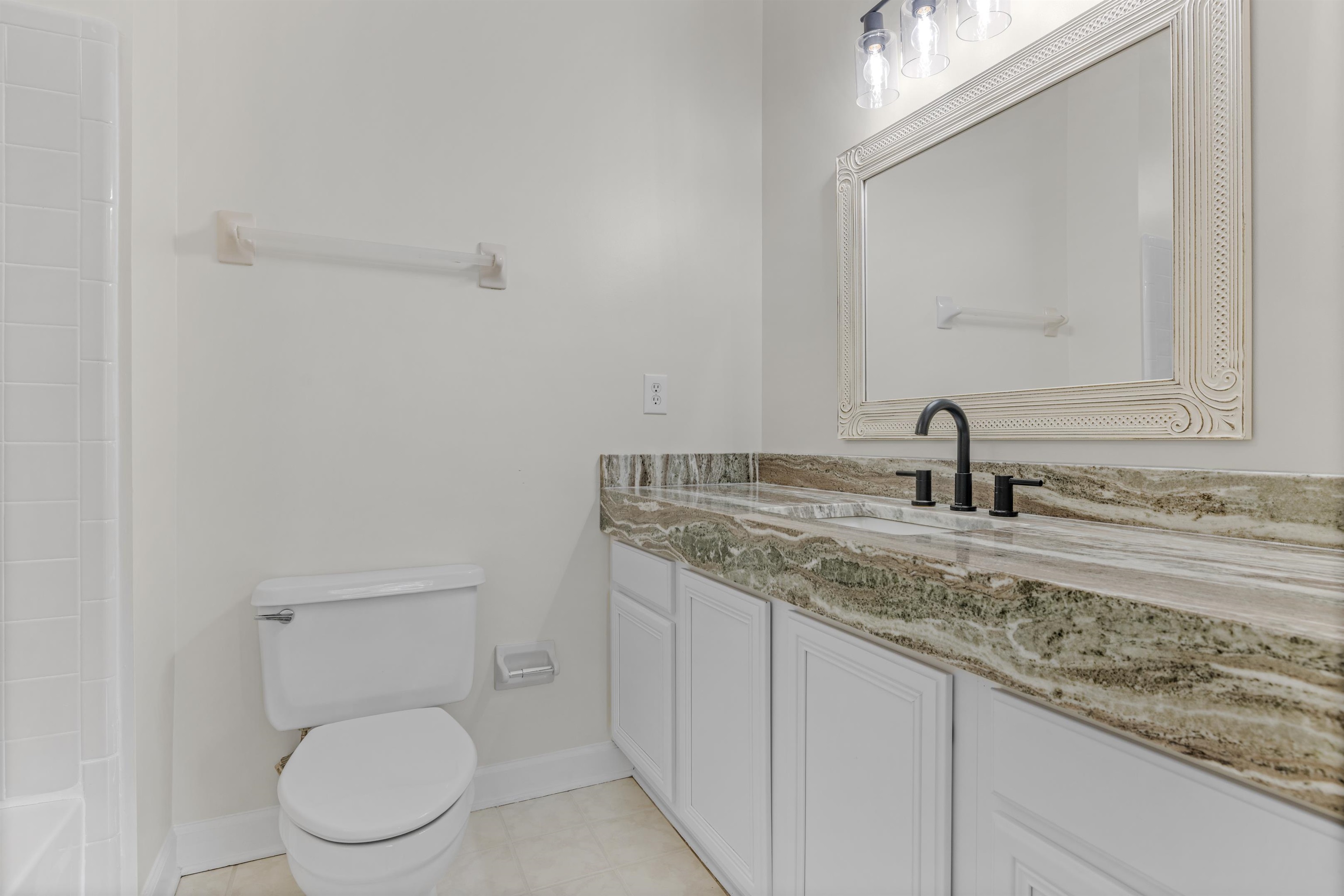 921 Harbor View Drive Memphis, TN 38103 - Photo 4 of 33 Bathroom featuring a vanity with a multi-toned stone countertop, a rectangular mirror with an ornate frame, a black-finish faucet, and white cabinetry