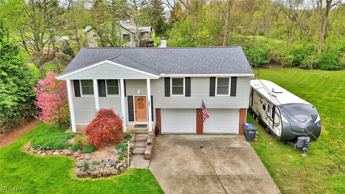 Bi-level home featuring a shingled roof, brick siding, a garage, a front yard, and concrete driveway