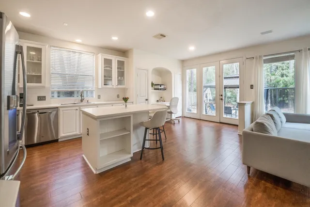 a living room with stainless steel appliances granite countertop a sink a stove a dining table and wooden floor