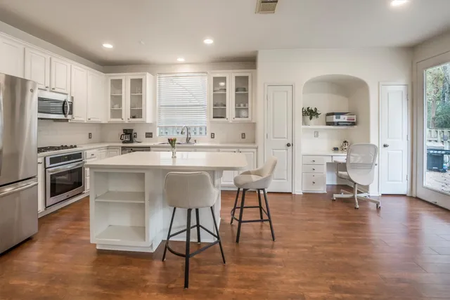 a kitchen with stainless steel appliances kitchen island granite countertop a stove a sink a refrigerator cabinets and a dining table with wooden floor