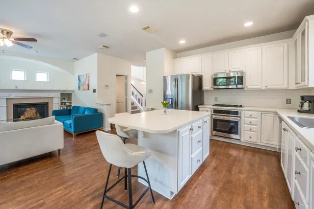 a kitchen with stainless steel appliances granite countertop a stove a sink dishwasher a microwave oven and a dining table with wooden floor