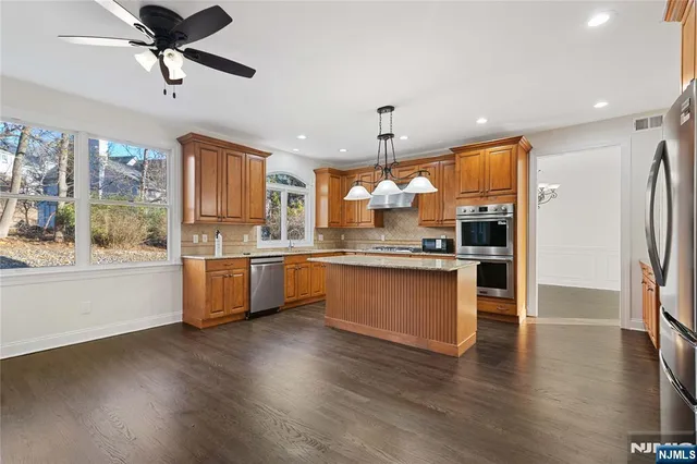 a kitchen with stainless steel appliances kitchen island granite countertop a refrigerator a oven a stove and a wooden floors