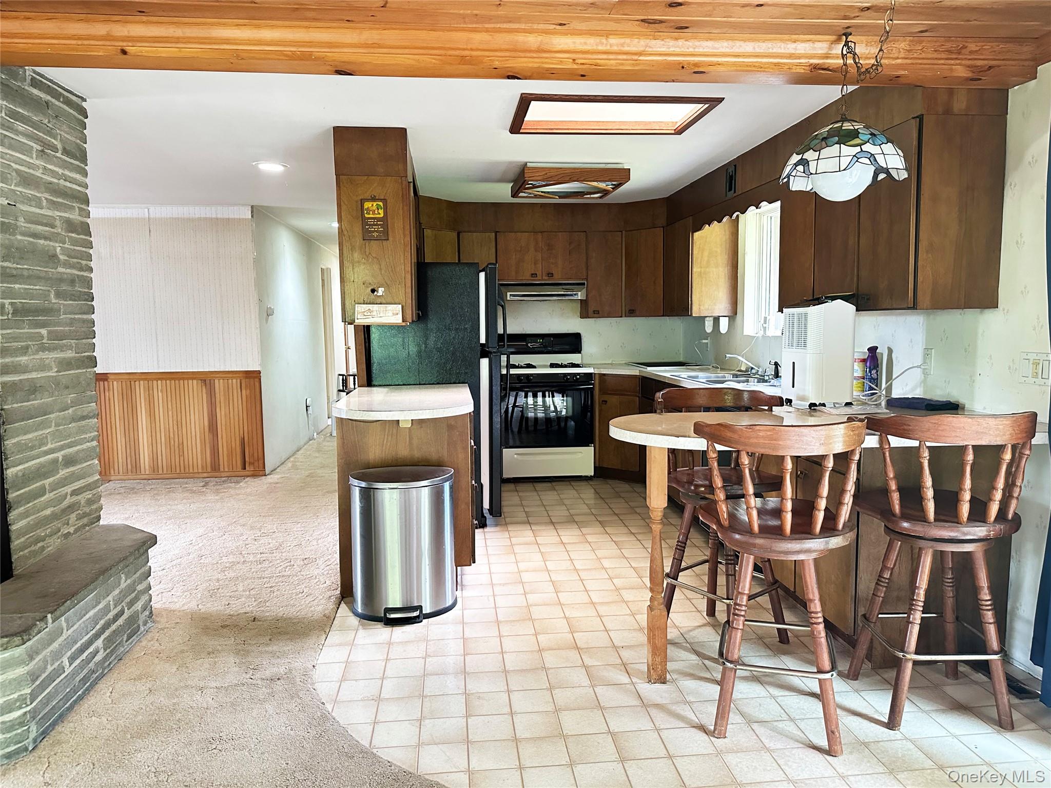 818 Methol Road Roscoe, NY 12776 - Photo 26 of 39 Rustic kitchen and dining area with wood cabinetry, skylights, breakfast seating, and open connection to the main living space.