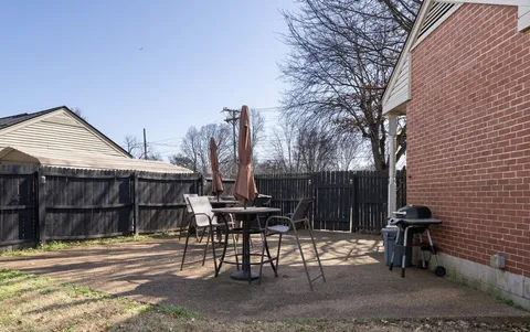 a view of a patio with table and chairs with wooden fence and large trees