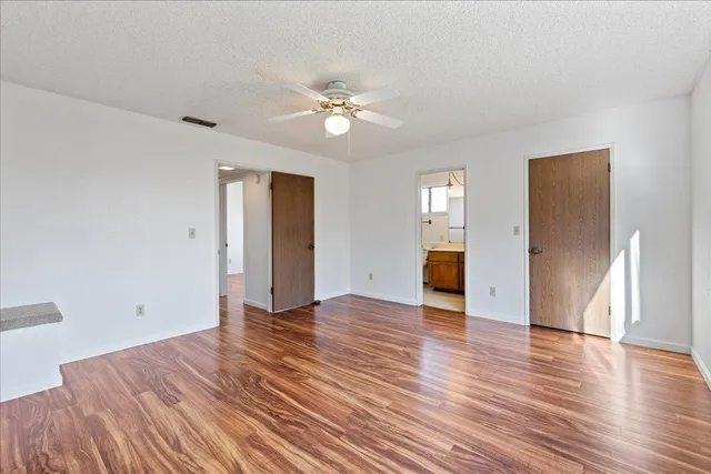 a view of an empty room with wooden floor and a ceiling fan
