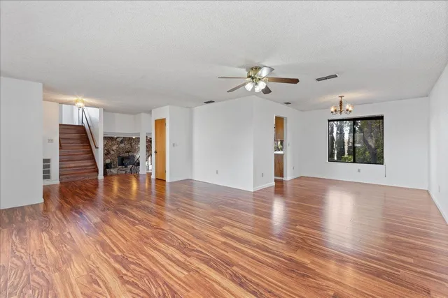 a view of an empty room with wooden floor and a ceiling fan