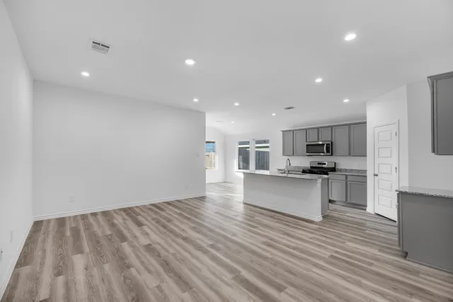 a view of kitchen with microwave oven a stove and white cabinets with wooden floor