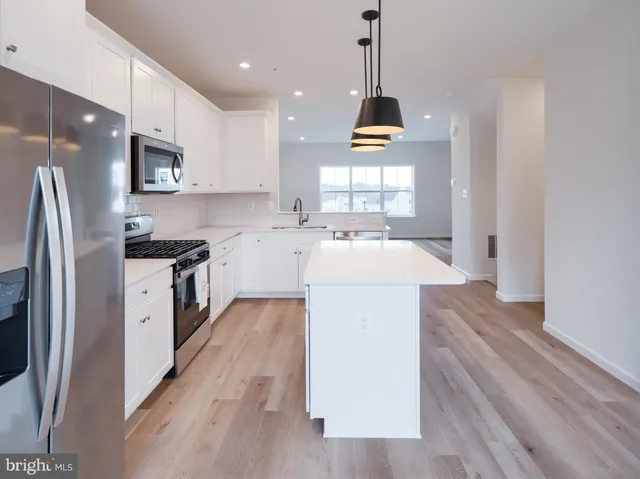 a kitchen with stainless steel appliances granite countertop a refrigerator a sink dishwasher a stove and white countertops with wooden floor