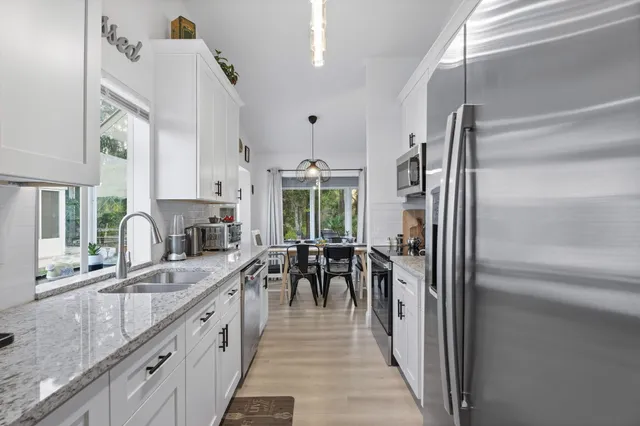 a kitchen with stainless steel appliances granite countertop a refrigerator a sink dishwasher a stove and a dining table with wooden floor