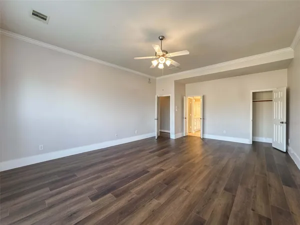 a view of an empty room with wooden floor and fan
