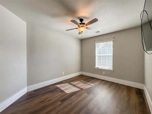 an empty room with wooden floor fan and windows