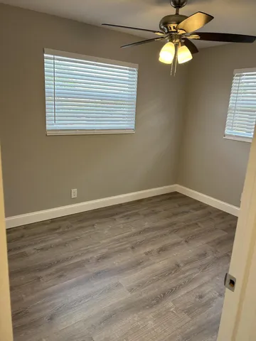 an empty room with wooden floor fan and windows