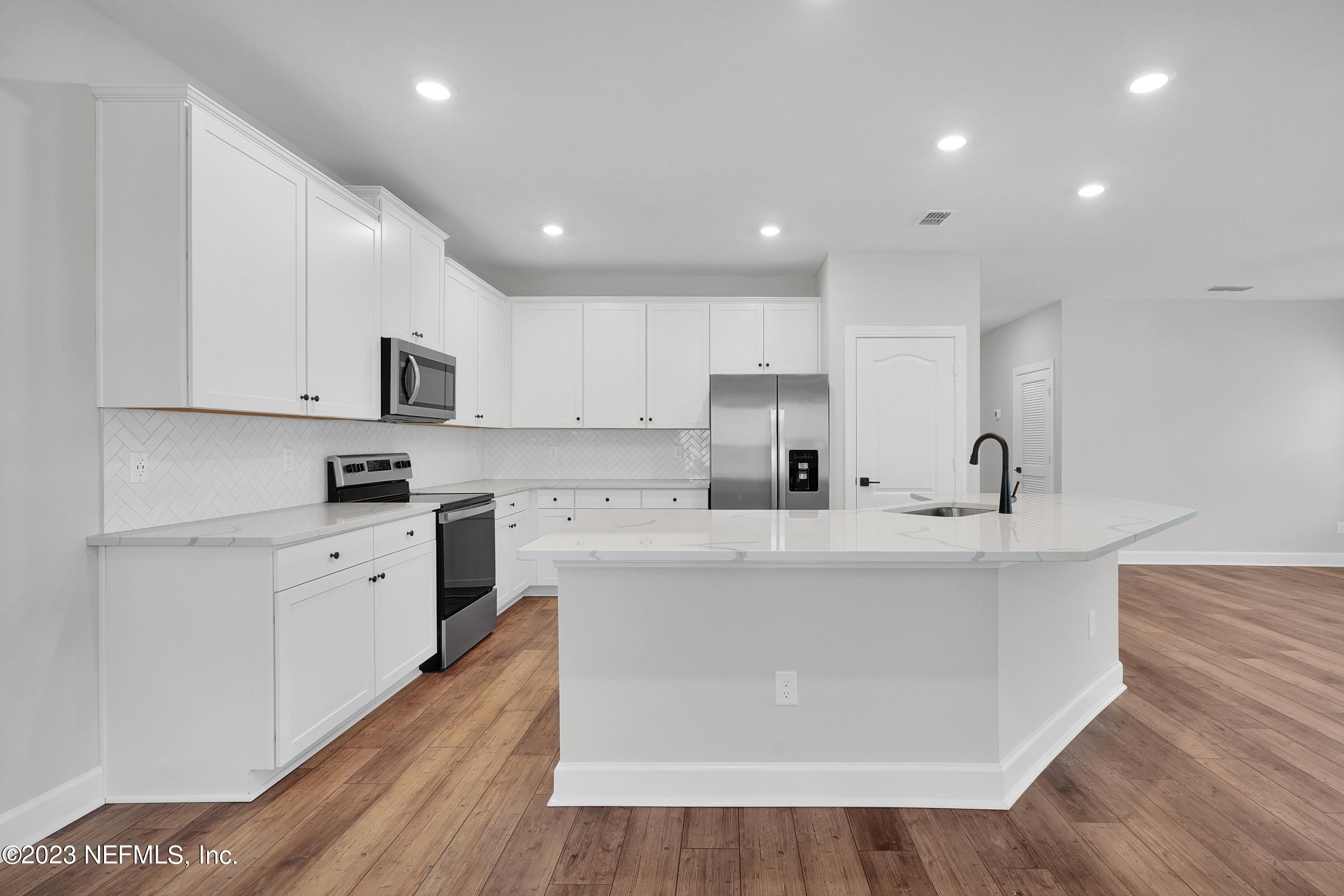 654 Morgans Treasure Road St. Augustine, FL 32084 - Photo 3 of 8 a large white kitchen with stainless steel appliances granite countertop a stove a sink a refrigerator and white cabinets with wooden floor